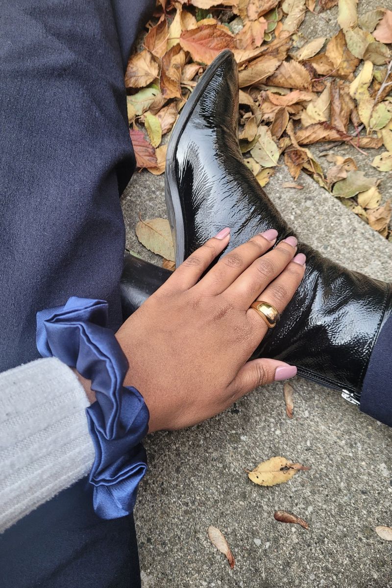 Midnight blue hair scrunchie worn on the wrist of someone sitting on fall leaves with their leather black boots