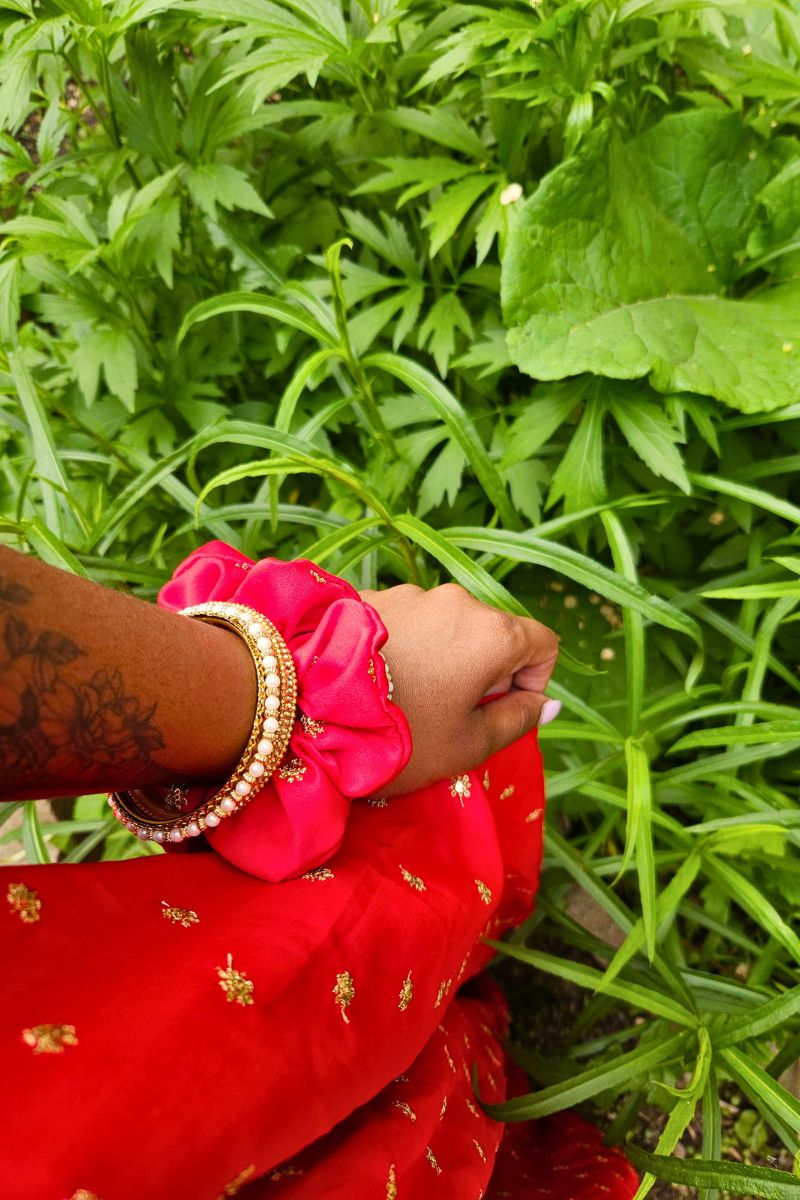 bright red hair scrunchie on a wrist with greenery in the background
